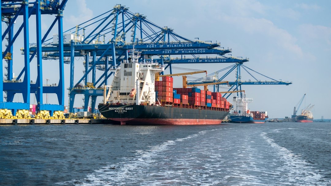 Container ship docked at an industrial port with gantry cranes.